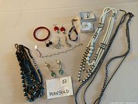 Photo showing an assortment of earrings, multiple necklaces, and a bangle bracelet spread on a surface