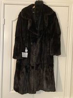 Full length shot of dark brown mink fur coat hung on a white door, showing overall condition and length.
