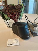 Tiffany style stained glass wastebasket with grape motif, black X-ACTO electric pencil sharpener, and silver and black electric stapler on a tabletop.