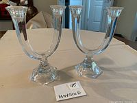 Two clear glass U-shaped candlesticks with two arms each and hexagonal bases shown upright on a table.