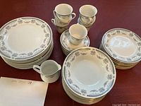 Set of stacked plates along with cups and small pitcher, showing the overall look of the dishes with light green floral pattern.