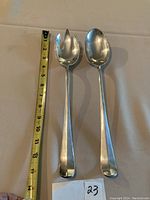 Pair of silver plated 13 inch salad servers showing front side with a measuring tape indicating length.