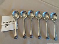 Top view of six silver spoons, evenly spaced with their bowls facing up, showing overall lot and condition.