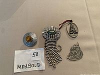 Lot showing all five items together on a beige cloth: sterling Celtic brooch with yellow stone, rhinestone brooch with fringe, and two pewter Christmas ornaments.