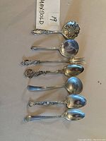 Overview of all seven sterling silver serving utensils on fabric background
