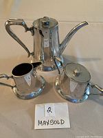 Three-piece set displayed on table: coffee pot, creamer, sugar bowl with lids
