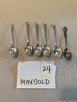 Six sterling silver coffee spoons laid out, five spoons with matching plain pattern and one ornate spoon at right end.