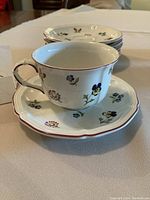 Close-up of cup and saucer showcasing floral design, scalloped edges, and red rim detailing.