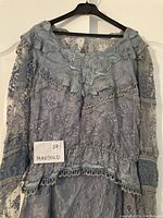 Gray lace long sleeve blouse and skirt set hanging on a hanger, showing ruffled details, floral lace applique on blouse, and lace pattern on skirt