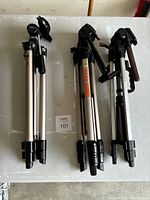 Photo of three folded camera tripods side by side on a gray surface showing their legs and heads.