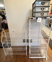 Three white wire storage units arranged next to a wall including a tall unit with four metal drawers and two smaller wire units.