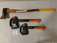Full view of three tools: Yardworks 33 inch splitting maul with wooden handle, Fiskars X7 hatchet and Fiskars X11 splitting axe with plastic handles and guards.