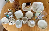 Full view of assorted dishware including plates, mugs, pitchers, various glasses on a wooden table.