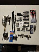 Photo of assorted drill bits, screw extractors, and bit holders laid out on table.