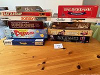 Photo showing a collection of boxed vintage board games including Battleship, Clue, Sorry, Balderdash, Ouija, Super Quiz, Perfection, Electronic Game, Challenge Yahtzee, and Swoggle arranged on a wooden surface.