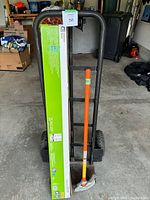 Metal hand truck front view with two pneumatic wheels, rusted base, tagged with item 58 label, showing the conduit bender and LED shoplight box leaning against it.