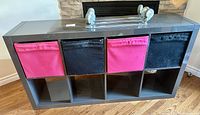 Front view of grey IKEA storage unit with four cloth drawers, two pink and two black, placed in alternating order, with some visible marks and damage
