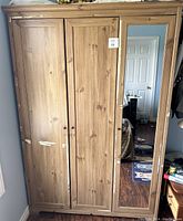Front view of wooden wardrobe with three doors; right door has full-length mirror. Visible scuffs and paint chips on the wood finish.