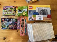 Overview photo of all items in the lot showing sealed LEGO polybags, LEGO picture frame set box, LEGO DOTS items, and IKEA LEGO storage box with base plates.