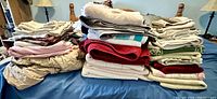 Wide shot of all stacked linens, showing multiple piles of towels and sheets in various colors and sizes on a bed.