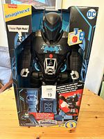 Front view of Bat-Tech Batbot in box showing robot mode with blue bat symbol and interactive button.