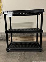 Front view of black three-shelf shelving unit showing open grid shelves and general condition.