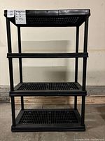 Front view of the 4-shelf black plastic shelving unit showing the slatted shelves and vertical support posts.