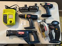 Layout of kit with yellow Ryobi charger, two batteries, drill, impact driver, reciprocating saw, circular saw, and carrying bag.