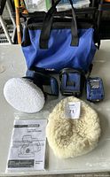View of Simoniz cordless polisher with white polishing pad attached, charger, battery, carrying bag and instruction manual.