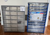 Two storage drawer units side-by-side on the floor: a taller blue metal frame Mastercraft parts cabinet with 43 drawers shrink-wrapped, and a shorter plastic cabinet with 18 clear drawers, some pulled out and one resting on top.