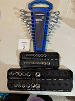 Photo of the full set including 9 wrenches displayed in a blue triangular holder, 31 sockets organized in three black trays, and three blue plastic organizers.