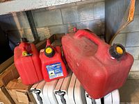 Three red plastic gas cans on white folding chairs against concrete wall