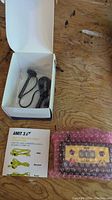 Photo of AMIT 3.0 device wrapped in bubble wrap with manual and cables next to open box.