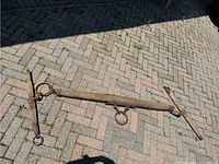Antique horse yoke made of wood and iron lying on a paved surface, showing iron fittings and central ring.