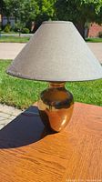 Brass side lamp displayed on a wooden surface outside with natural daylight. Shows the lamp in good condition, visible dent on brass base is not prominent from this angle.