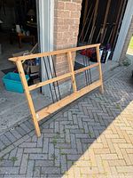 Ikea Dalselv queen size headboard made of wood frame with vertical black metal rods, standing outside a garage on a driveway.