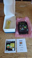 Nayax VPOS credit card reader, yellow power cable in box, and payment instruction cards on wooden surface