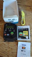 Nayax VPOS credit card reader, box, yellow Ethernet cable, and initial instruction manuals placed on a wooden surface.