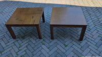 Two square oak wood tables on pavement, showing wood grain and condition.
