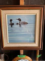 Framed print of two loons on a lake with wood and beige fabric mat frame, front view