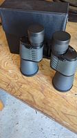 Black Rokinon binoculars resting on wooden surface, with lens caps fitted and black carrying case in background.