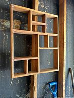 Frontal view of wooden wall-mounted trinket display with assorted compartments on a rustic dark wall background.