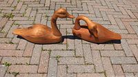 Side view of two carved wood Canada geese positioned on brick pavement showing their profile and condition.