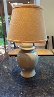Photo of the vintage ceramic lamp with burlap shade on a dark countertop in natural light, showing lamp details and size.