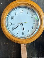 Front view of the wooden framed wall clock showing the clock face with Arabic numerals and hands indicating the time.