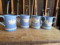 Four blue Jasperware Wedgwood mugs in a row each with white panels and white decorative borders, depicting London landmarks and Christmas year plaques.