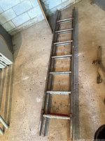 Full length view of the wooden expandable ladder lying flat on floor showing overall shape and construction with metal attachments at ends.