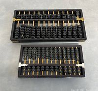 Two vintage abacuses on a grey surface showing black frames and beads with wooden rods.