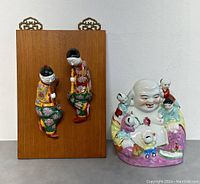 Two Famille Rose porcelain reclining figurines on a wooden board and the porcelain Laughing Fertility Buddha with children placed side by side.