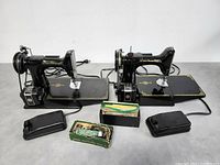 Two Singer Featherweight machines side by side with foot pedals, cords and accessory boxes